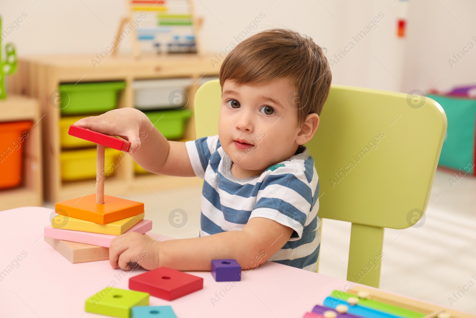 Photo of Little child playing with toy pyramid at table