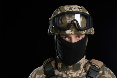 Soldier in Ukrainian military uniform with tactical goggles and balaclava on black background. Space for text