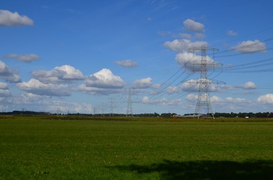 Photo of High voltage towers with electricity transmission power lines in field on sunny day