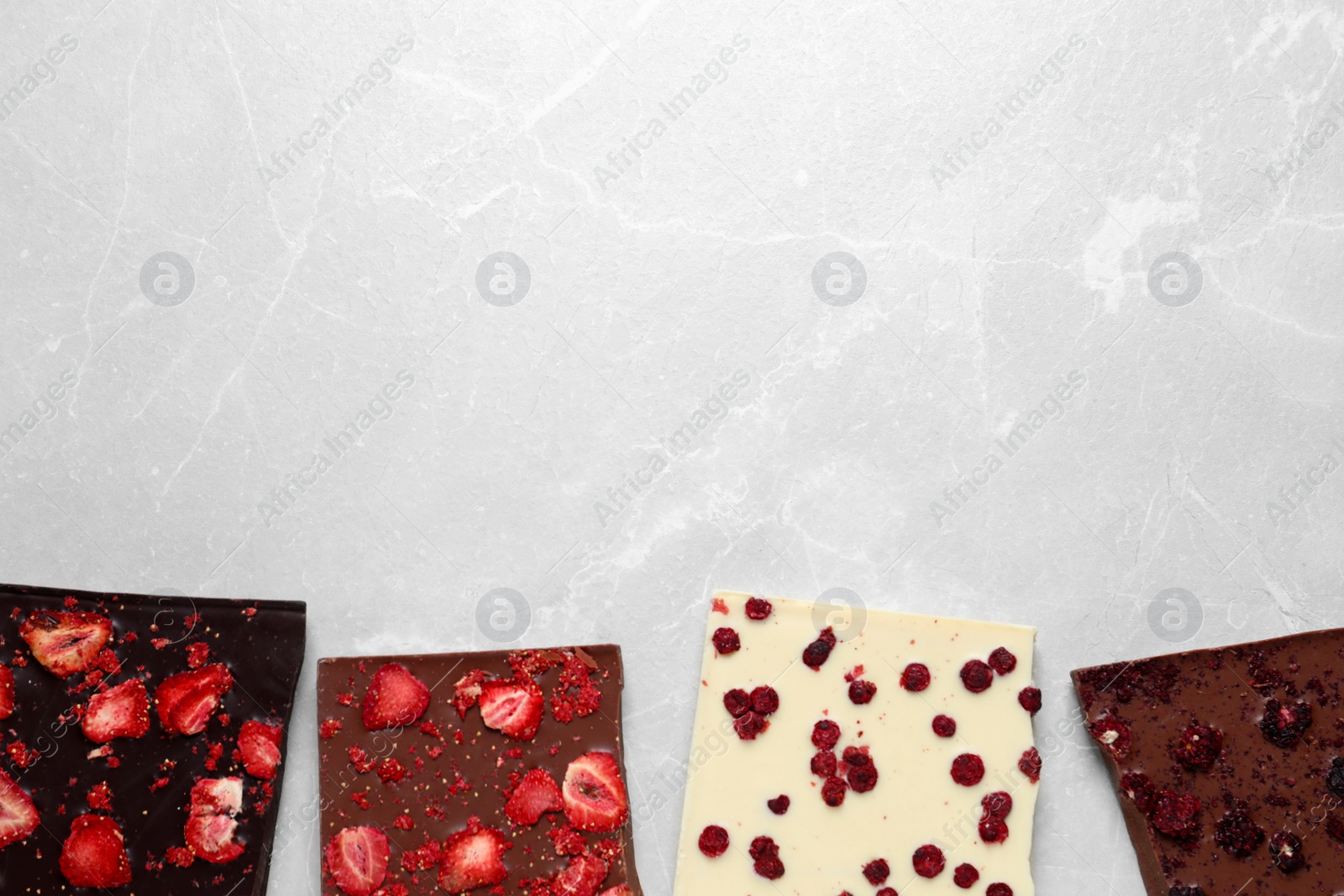 Photo of Different chocolate bars with freeze dried fruits on light marble table, flat lay. Space for text