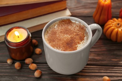 Photo of Cup of hot drink and burning candle on wooden table, closeup. Cozy autumn