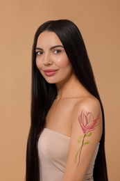 Young woman with tattoo of beautiful magnolia flower on beige background