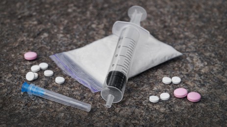 Photo of Plastic bag with powder, syringe and pills on stone surface, closeup. Hard drugs
