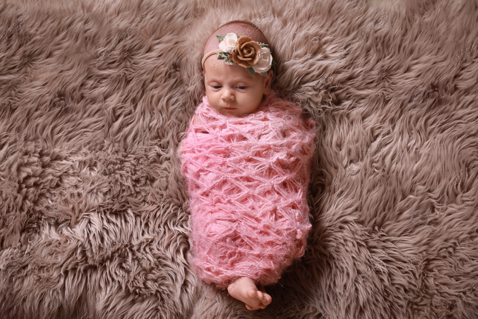 Photo of Cute newborn baby girl with floral headband lying on fuzzy rug, top view