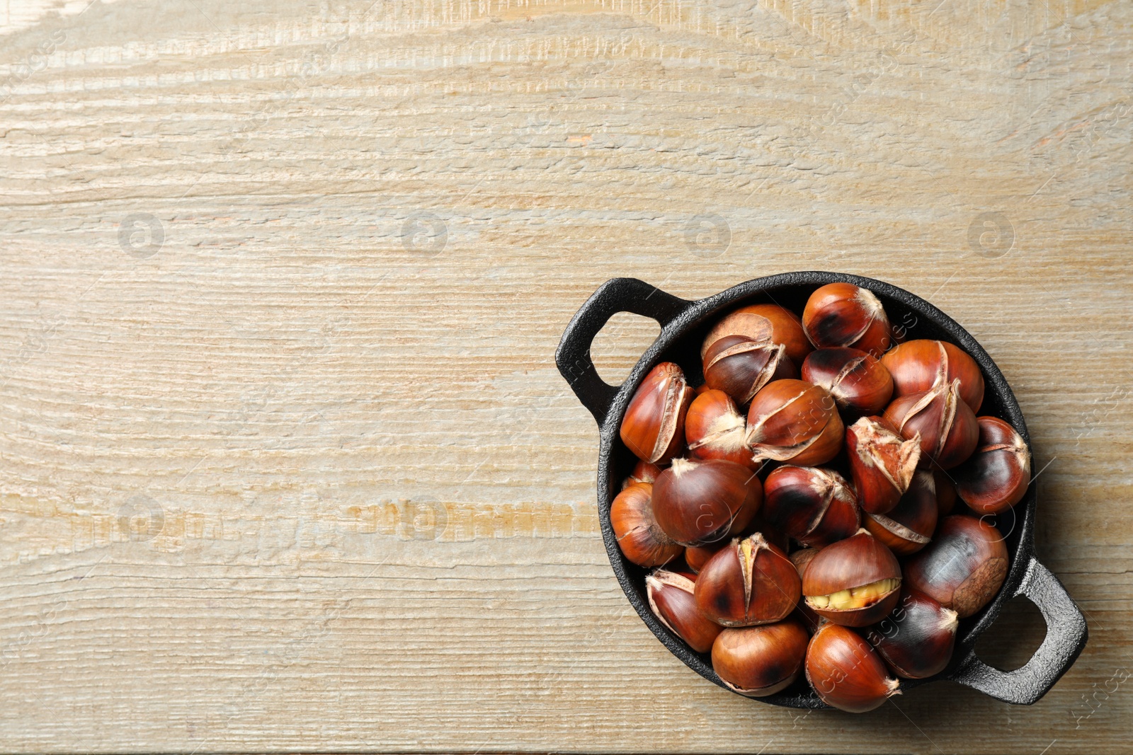 Photo of Tasty roasted edible chestnuts on wooden table, top view. Space for text