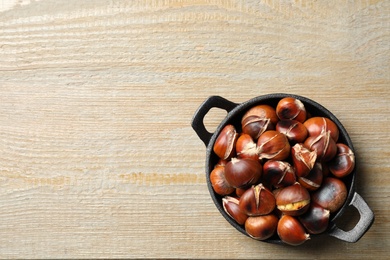 Photo of Tasty roasted edible chestnuts on wooden table, top view. Space for text