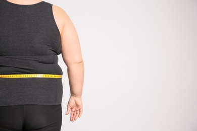 Photo of Overweight woman with measuring tape on light background