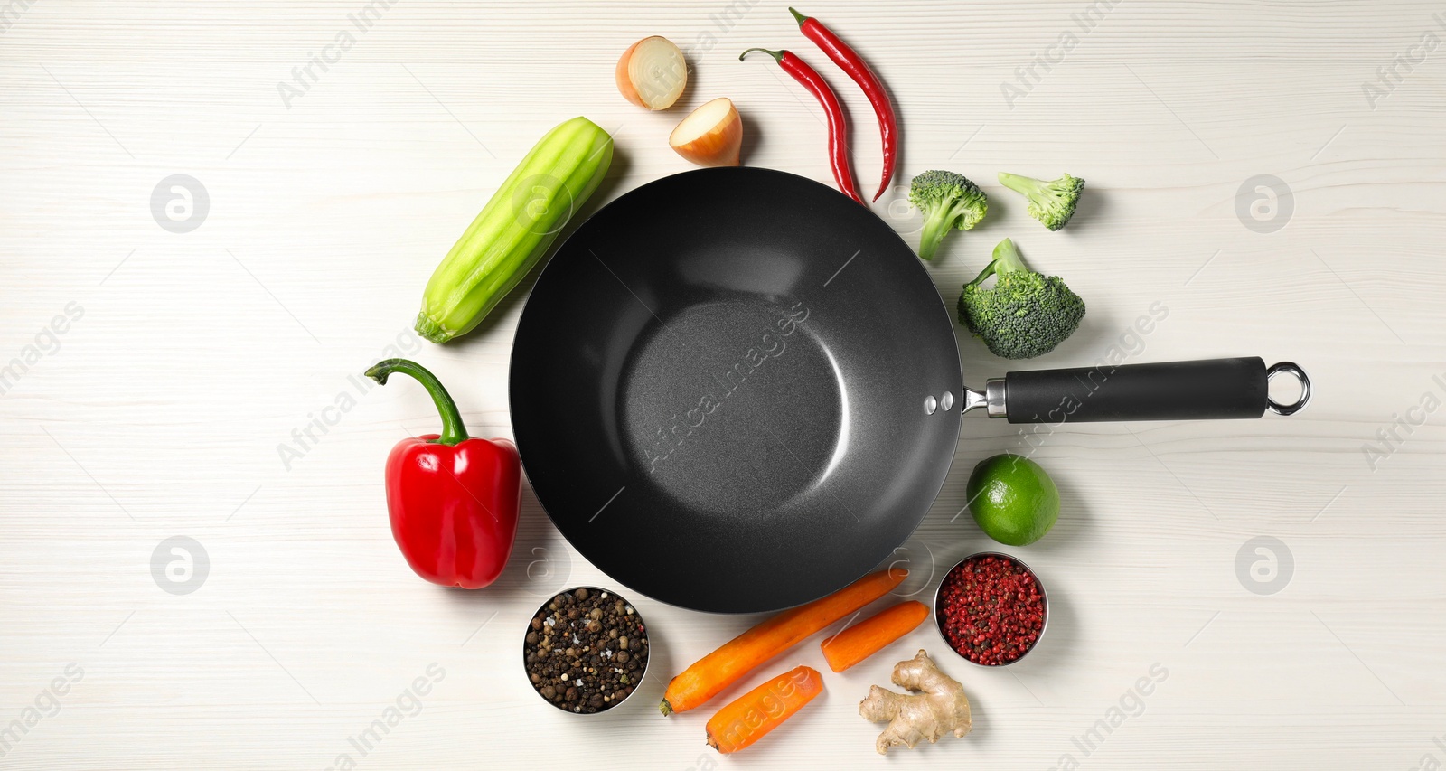 Photo of Empty iron wok surrounded by raw ingredients on white wooden table, flat lay