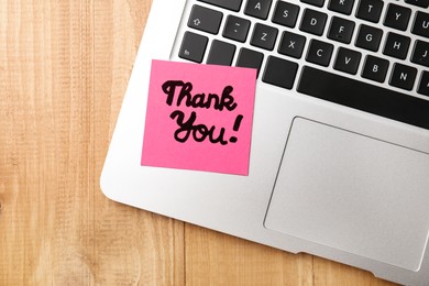 Photo of Pink paper note with phrase Thank You and laptop on wooden table, top view