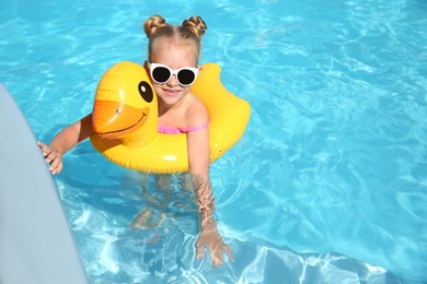 Photo of Happy little girl with inflatable ring in outdoor swimming pool on sunny summer day. Space for text