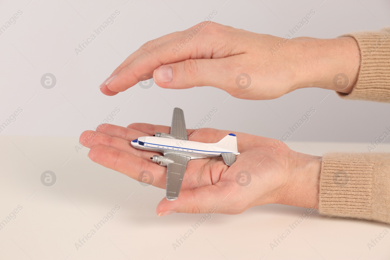 Photo of Woman covering toy plane on light background, closeup. Travel insurance concept