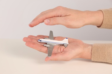 Photo of Woman covering toy plane on light background, closeup. Travel insurance concept