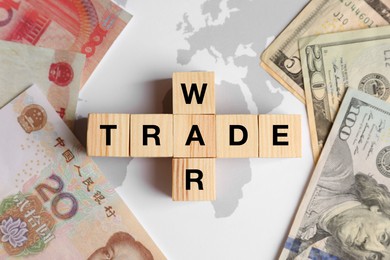Photo of Words Trade war made of wooden cubes, dollar and yuan banknotes on world map, flat lay