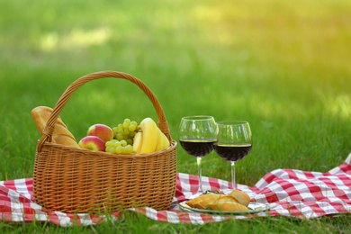 Photo of Wicker basket with food and wine on blanket in park, space for text. Summer picnic