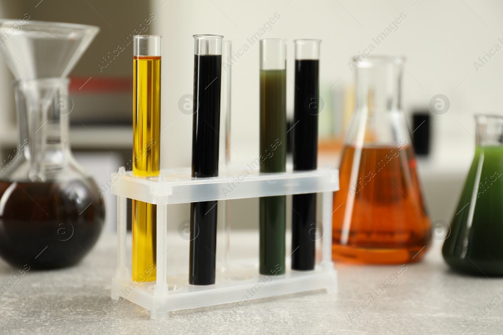 Photo of Laboratory glassware with different types of crude oil on light grey table