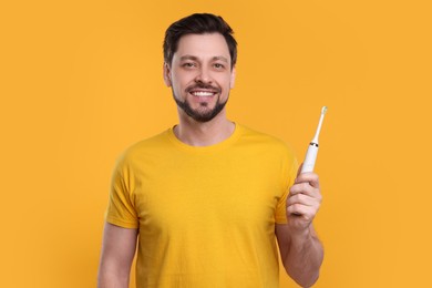 Photo of Happy man holding electric toothbrush on yellow background