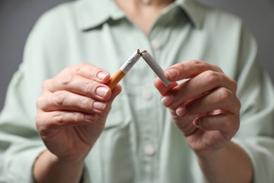 Photo of Stop smoking. Woman holding broken cigarette on grey background, closeup