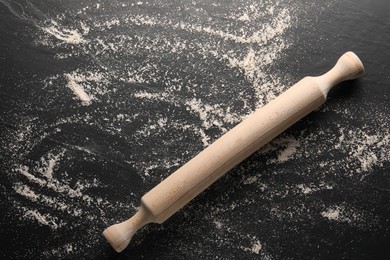 Photo of Scattered flour and rolling pin on black textured table, top view