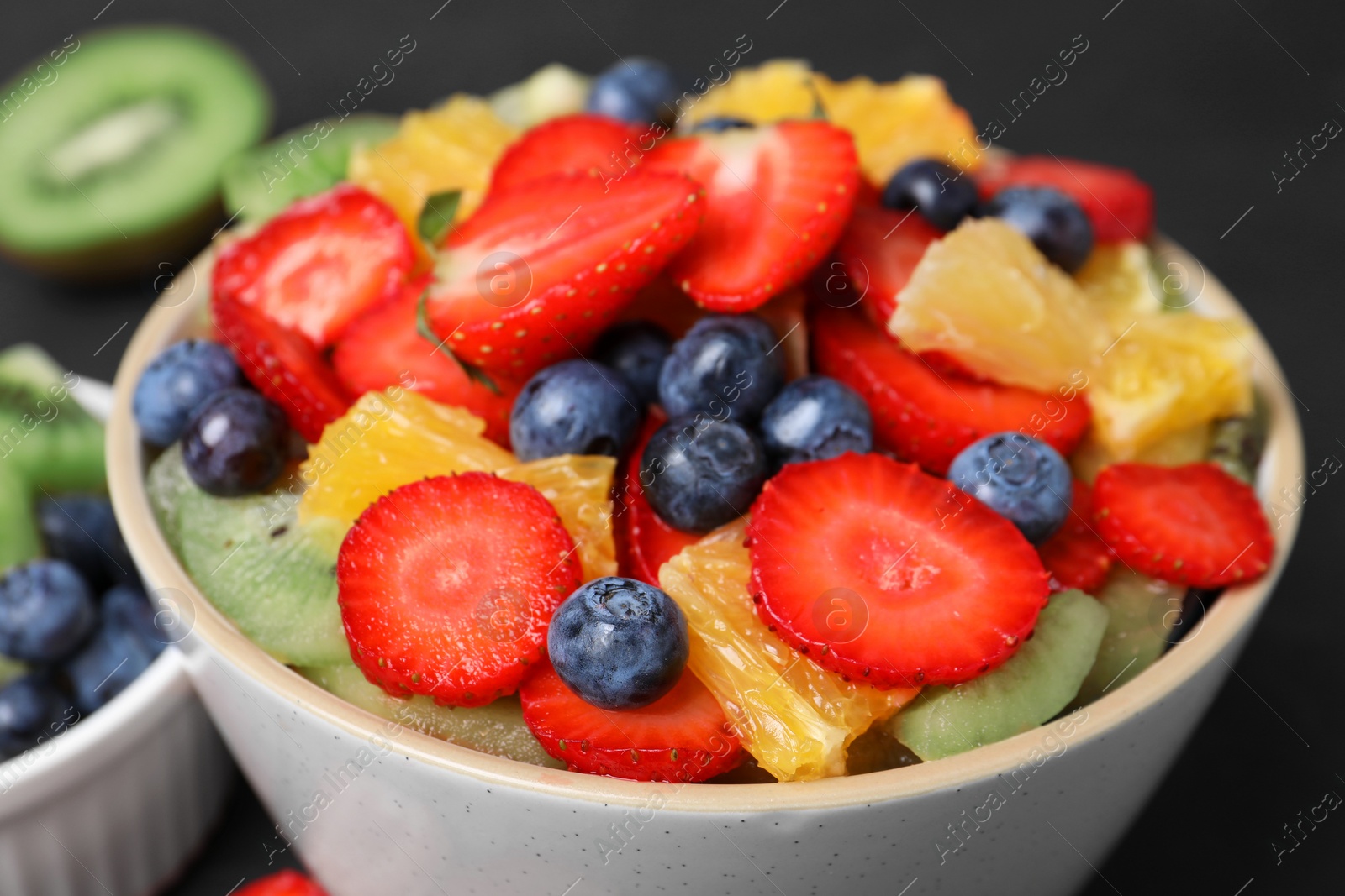 Photo of Delicious fresh fruit salad in bowl and ingredients on dark table, closeup