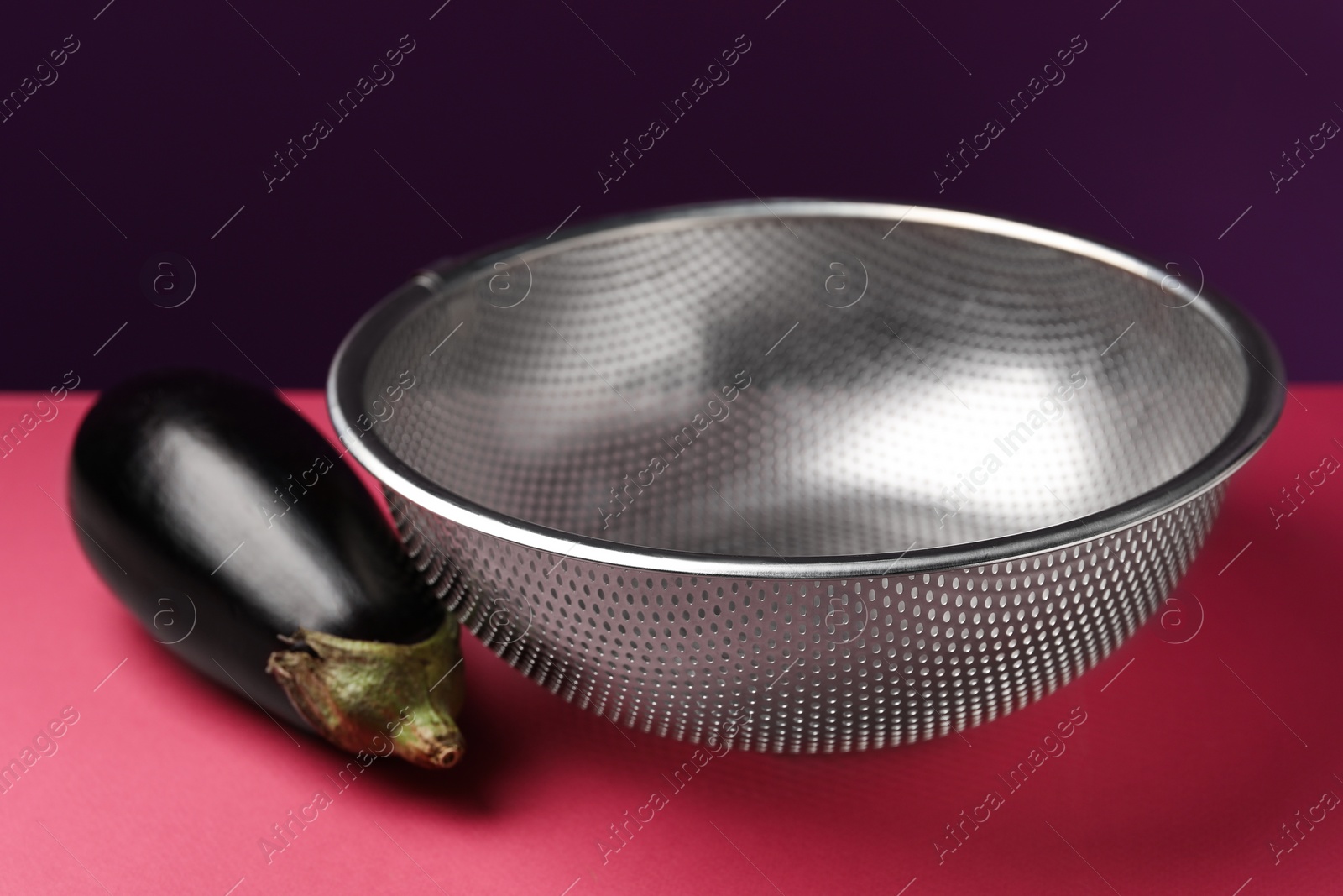 Photo of Colander with fresh eggplant on color background