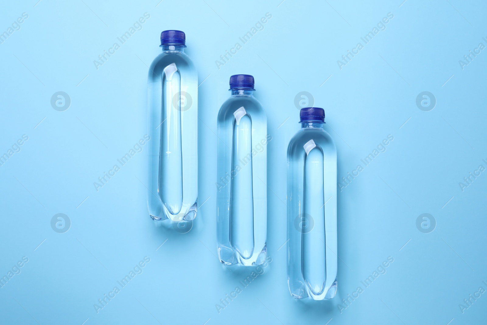 Photo of Plastic bottles with water on light blue background, flat lay