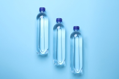 Plastic bottles with water on light blue background, flat lay