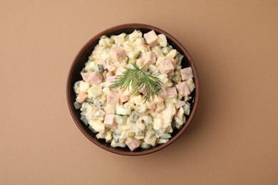 Photo of Tasty Olivier salad with boiled sausage in bowl on beige table, top view