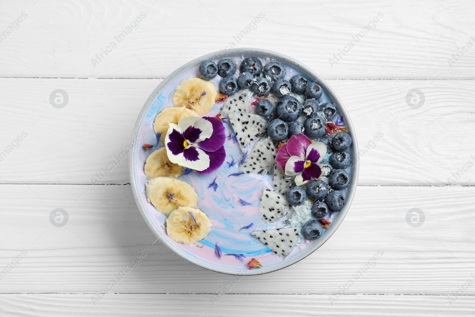 Photo of Delicious smoothie bowl with fresh fruits, blueberries and flowers on white wooden table, top view