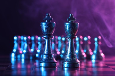 Photo of Kings in front of pawns on chessboard in color light, selective focus