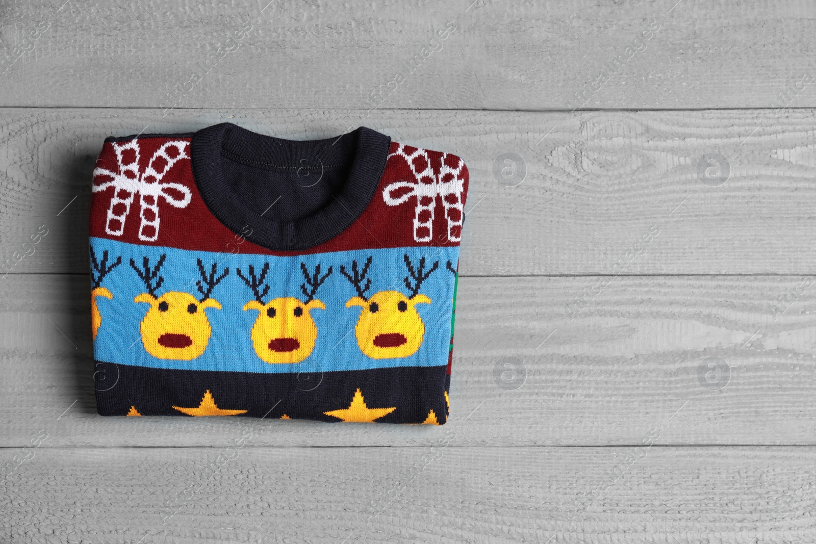 Photo of Warm folded Christmas sweater on grey wooden table, top view. Space for text