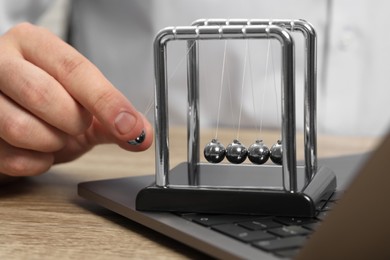 Photo of Man playing with Newton's cradle and laptop on wooden table, closeup. Physics law of energy conservation