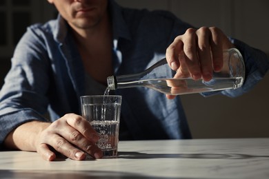 Photo of Addicted man with alcoholic drink at table in kitchen, closeup