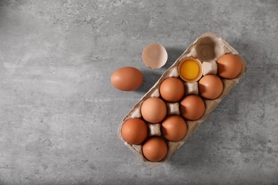 Fresh raw chicken eggs in carton on grey table, flat lay. Space for text