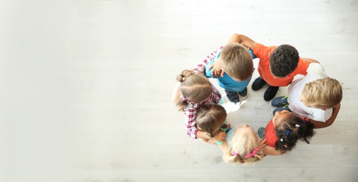 Photo of Little children making circle with hands around each other indoors, top view. Unity concept