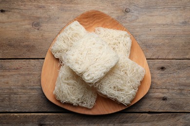 Plate with uncooked rice noodles on wooden table, top view