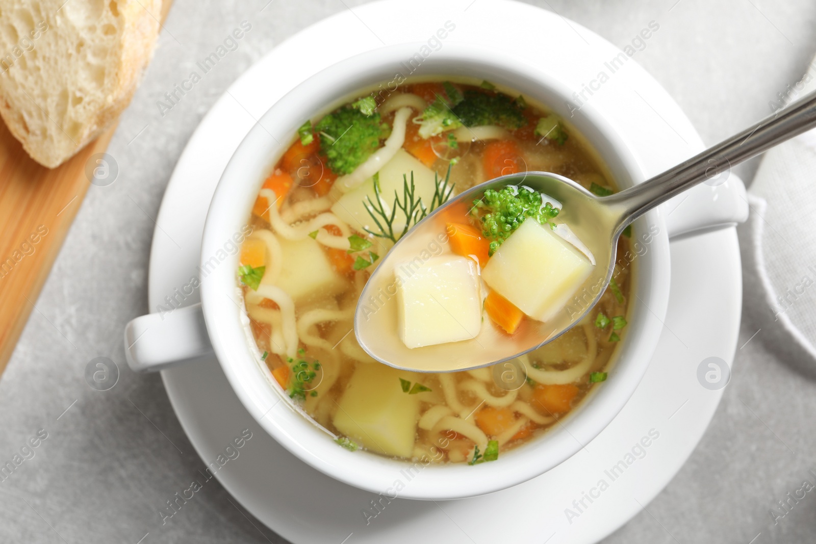 Photo of Spoon of fresh homemade vegetable soup over full dish on light grey table, top view