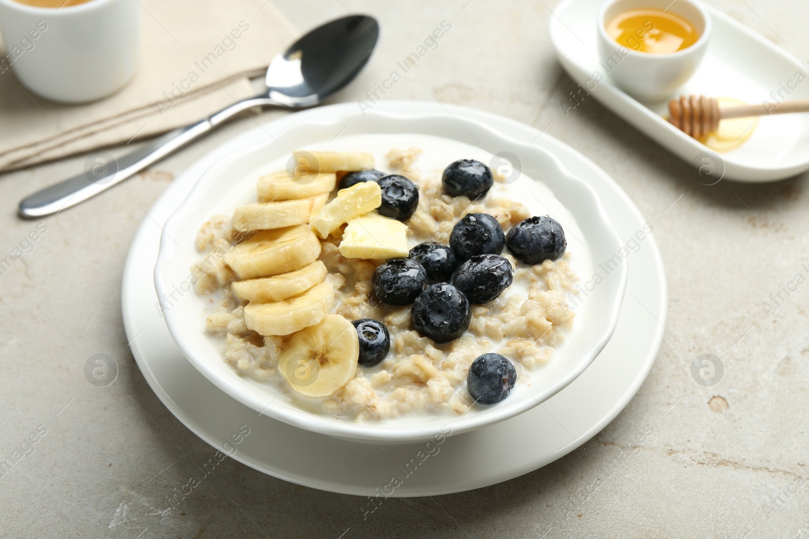 Photo of Tasty oatmeal with banana, blueberries, butter and milk served in bowl on light grey table