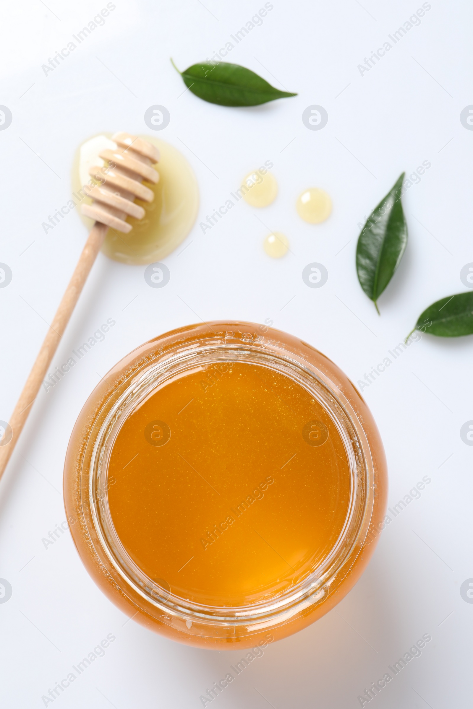 Photo of Tasty honey in glass jar, dipper and leaves isolated on white, top view