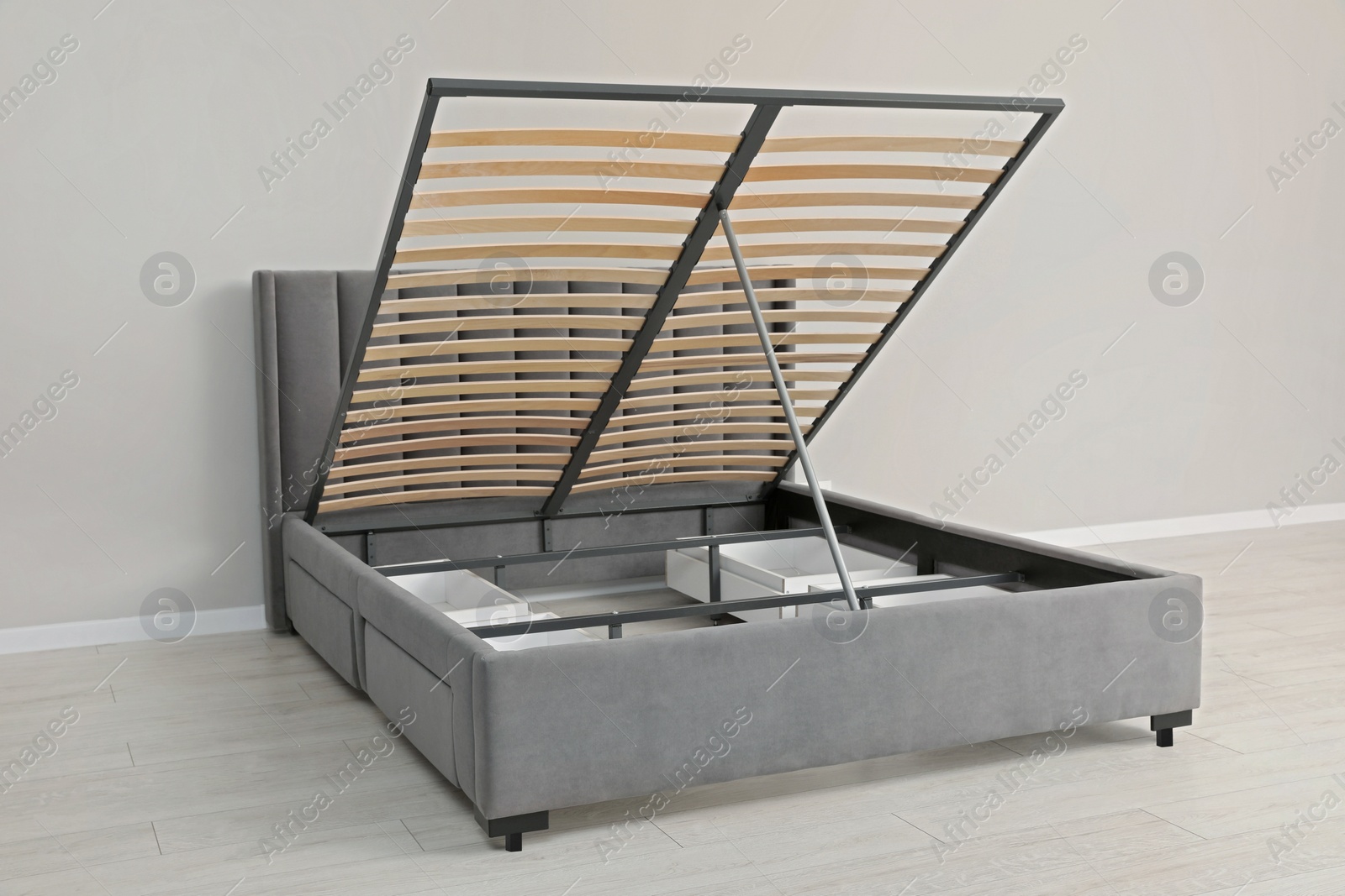 Photo of Comfortable bed with storage space for bedding under lifted slatted base in room