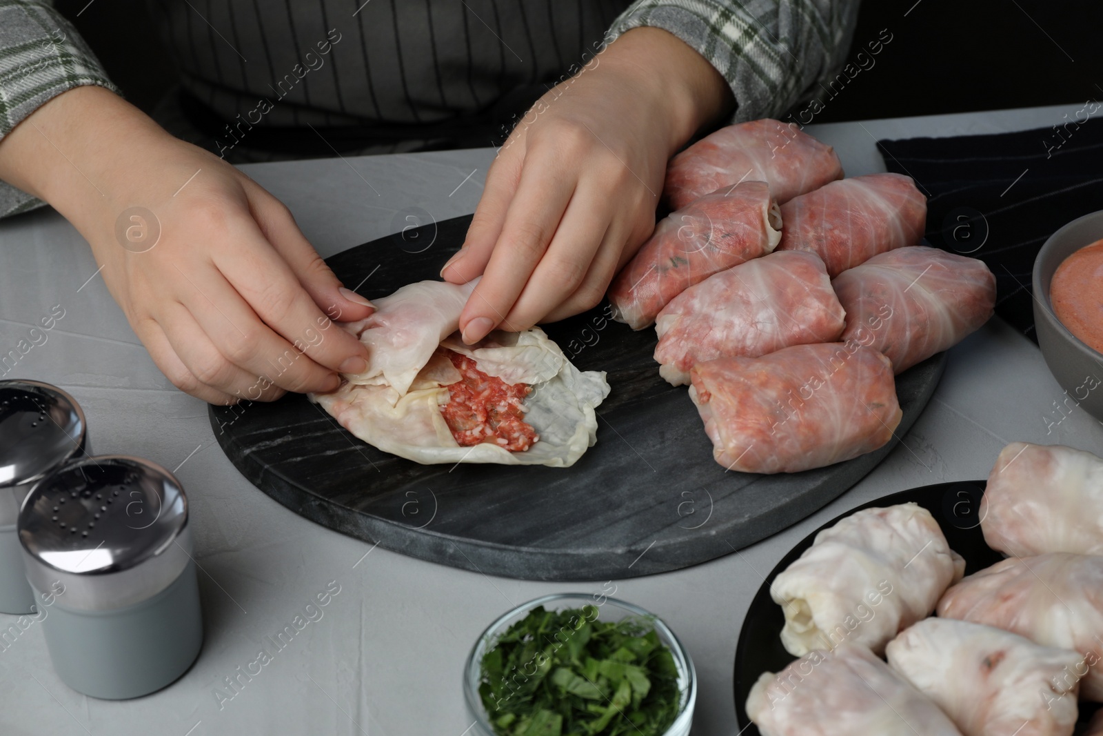 Photo of Woman making stuffed cabbage rolls at grey table, closeup