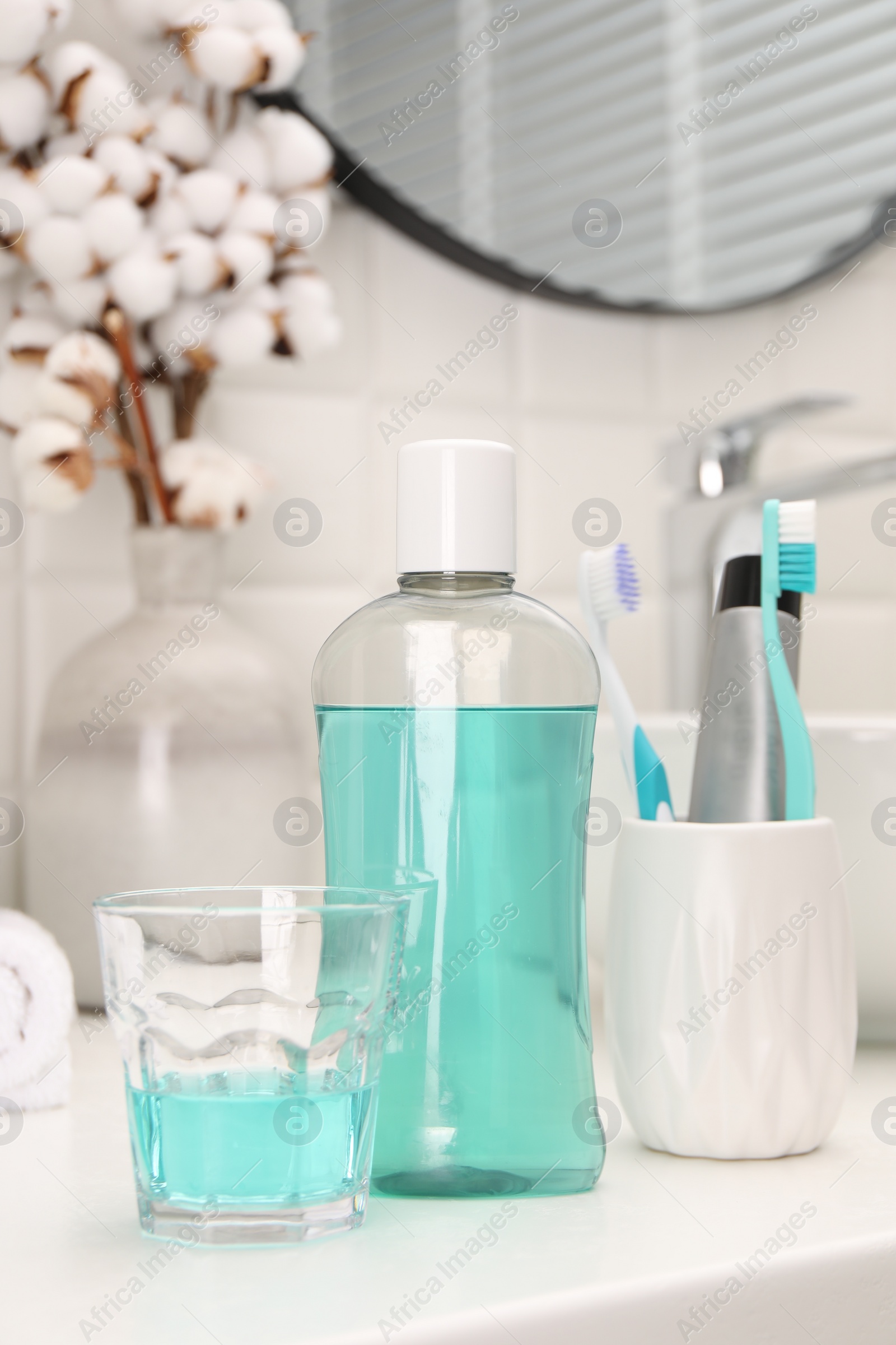 Photo of Bottle of mouthwash and glass on white table in bathroom