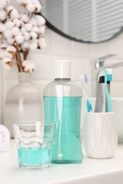 Bottle of mouthwash and glass on white table in bathroom