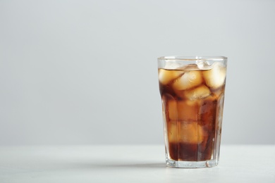 Photo of Glass of refreshing cola with ice cubes on table. Space for text