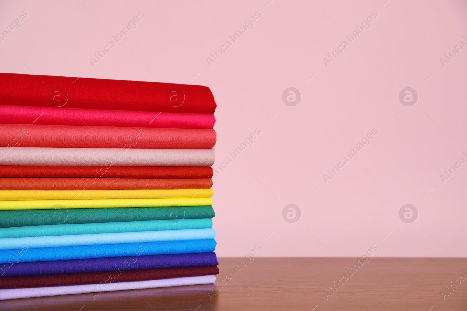 Photo of Pile of bright t-shirts on table against color background