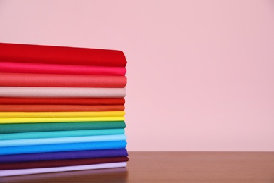 Photo of Pile of bright t-shirts on table against color background