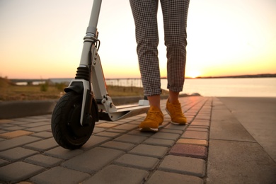 Woman with electric kick scooter outdoors at sunset, closeup