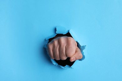 Photo of Man breaking through light blue paper with fist, closeup