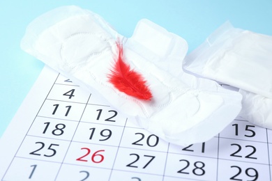 Menstrual pad with red feather and calendar on color background, closeup. Gynecological care