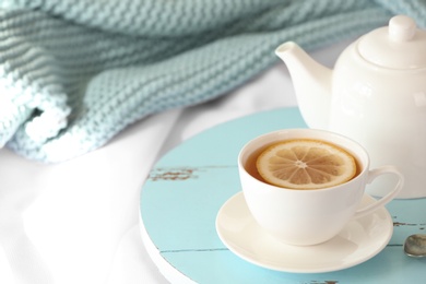 Wooden board with cup of lemon tea and teapot on fabric