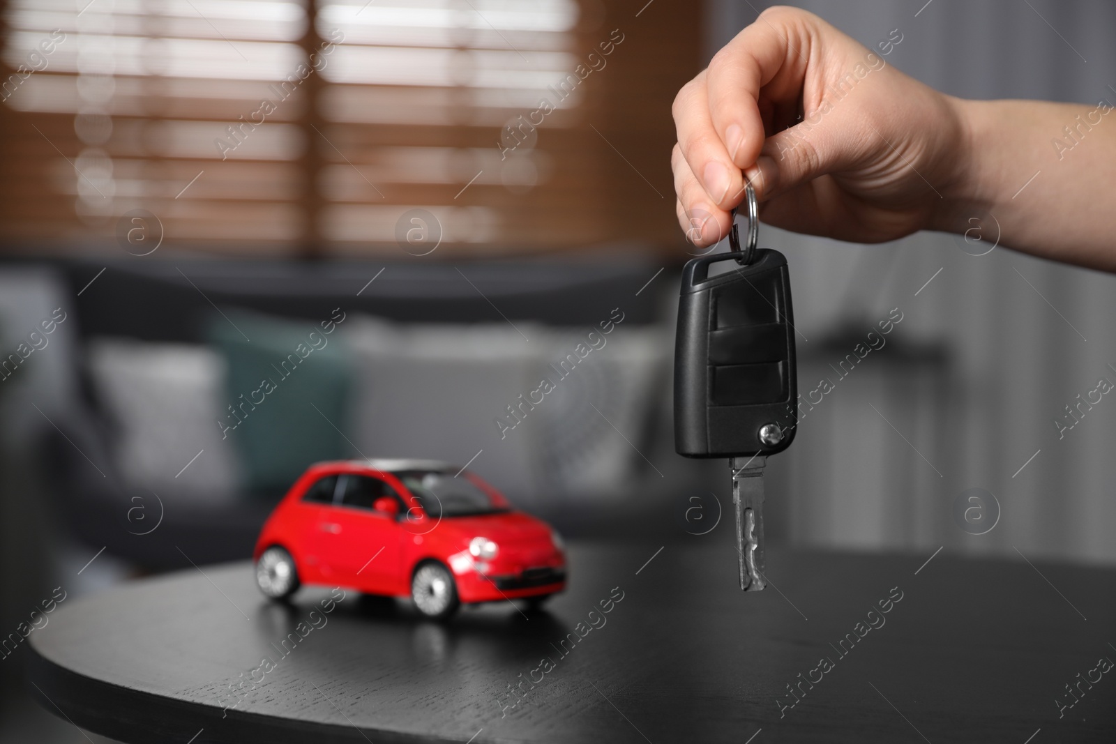 Photo of Man holding key near table with miniature automobile model indoors, closeup. Car buying